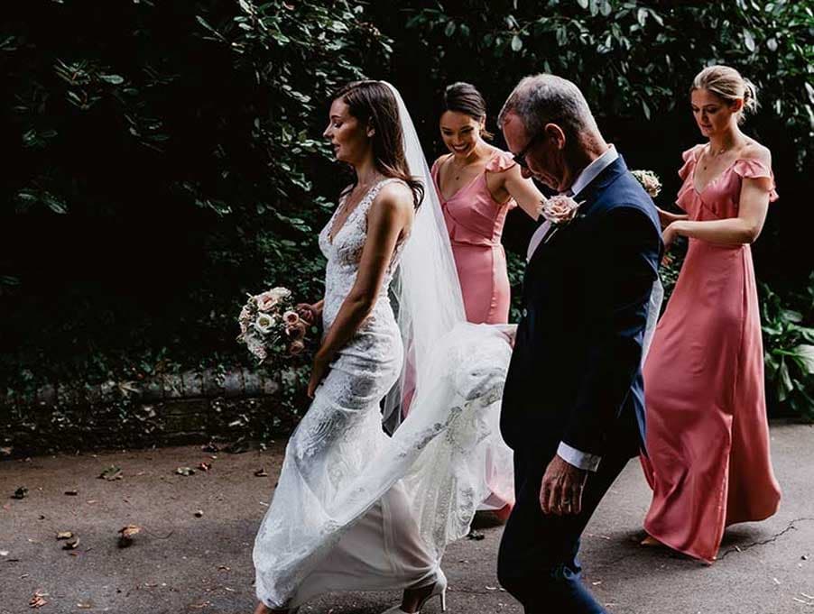 bride's dad and bridesmaids keep wedding dress lifted whilst walking towards the church