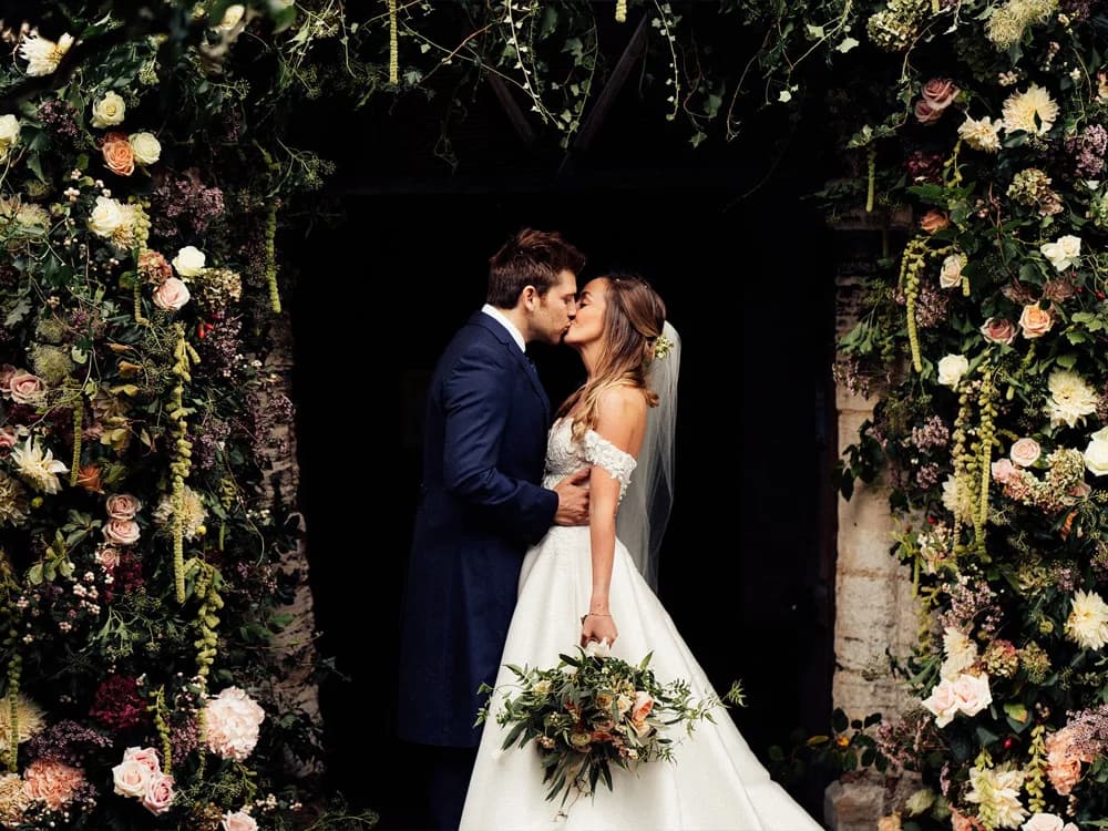 Bride and groom kiss under wedding flower arch