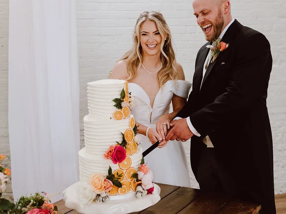 Couple cuts a three tier wedding cake decorated with flowers and fruit