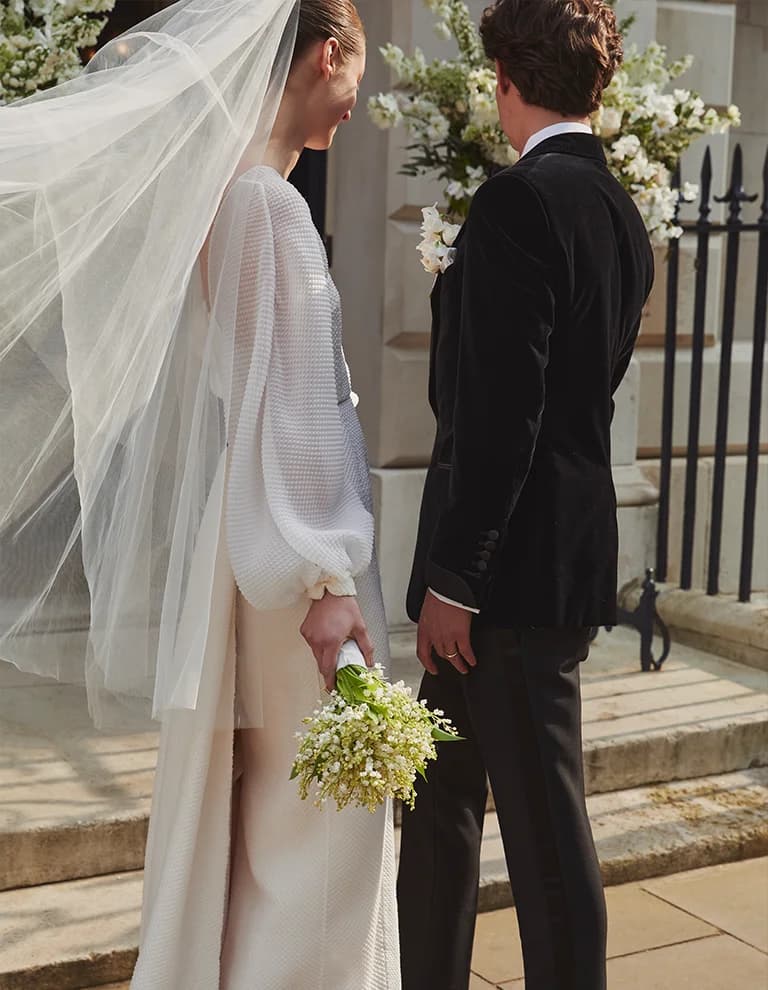 Groom and bride holding flower bouquet stand in front of the wedding venue