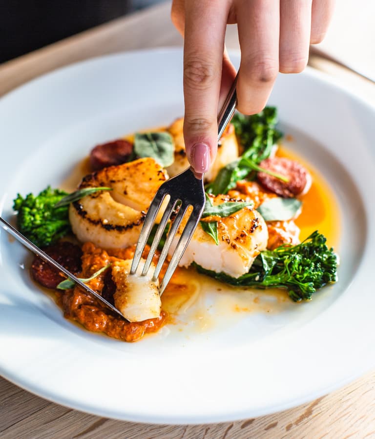 knife and fork picking up scallops with sauce