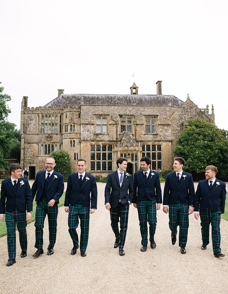 Groom and groomsmen in matchin suits walk outside the Brymton house wedding venue