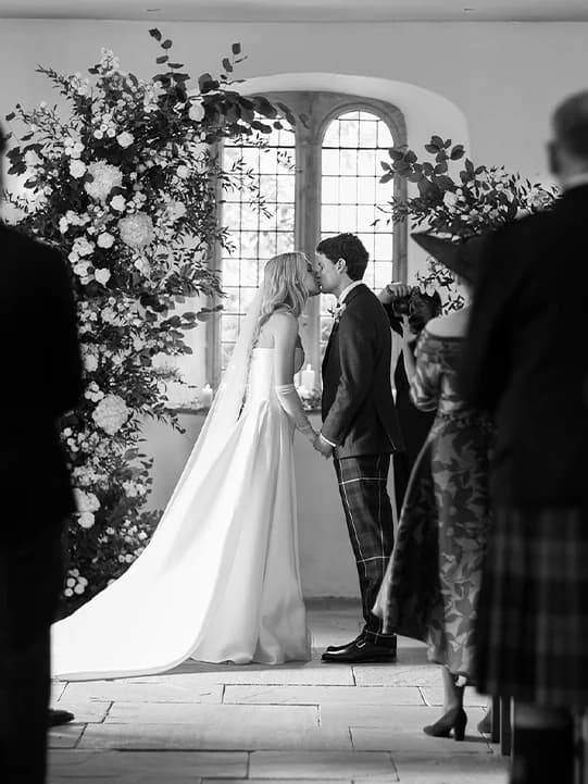 Bride and groom kissing during wedding ceremony among the delicate floral arches