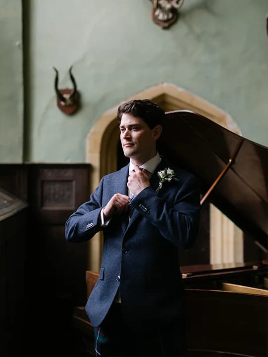 Groom fixing his shirt in the Brympton house ballroom
