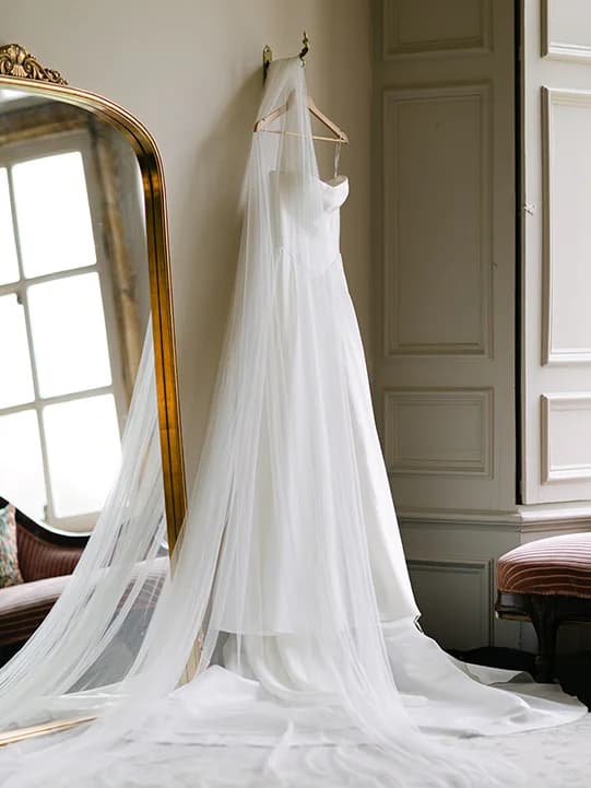 A wedding dress and veil hang on a mirror inside the bridal suite