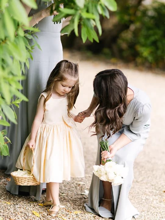 A bridesmaid with a flower girl in butter yellow dress holding a basket with confetti