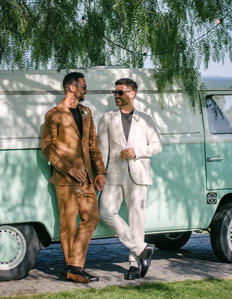 grooms in linen suits stand next to teal VW van