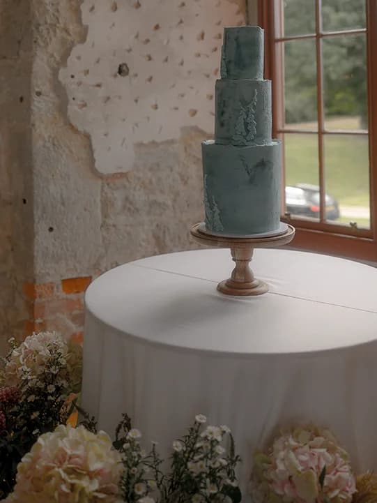 Blue three tier wedding cake placed on a table surrounded by flowers