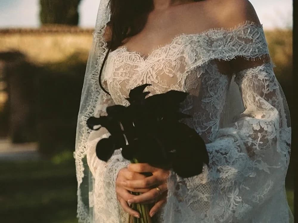 Bride in lace gothic-style wedding dress and veil holds black flowers