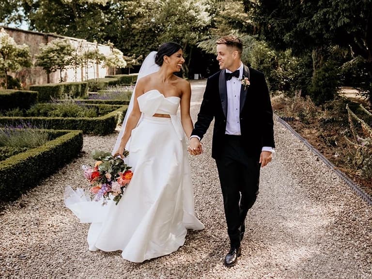 Bride and groom walk through the manor house garden