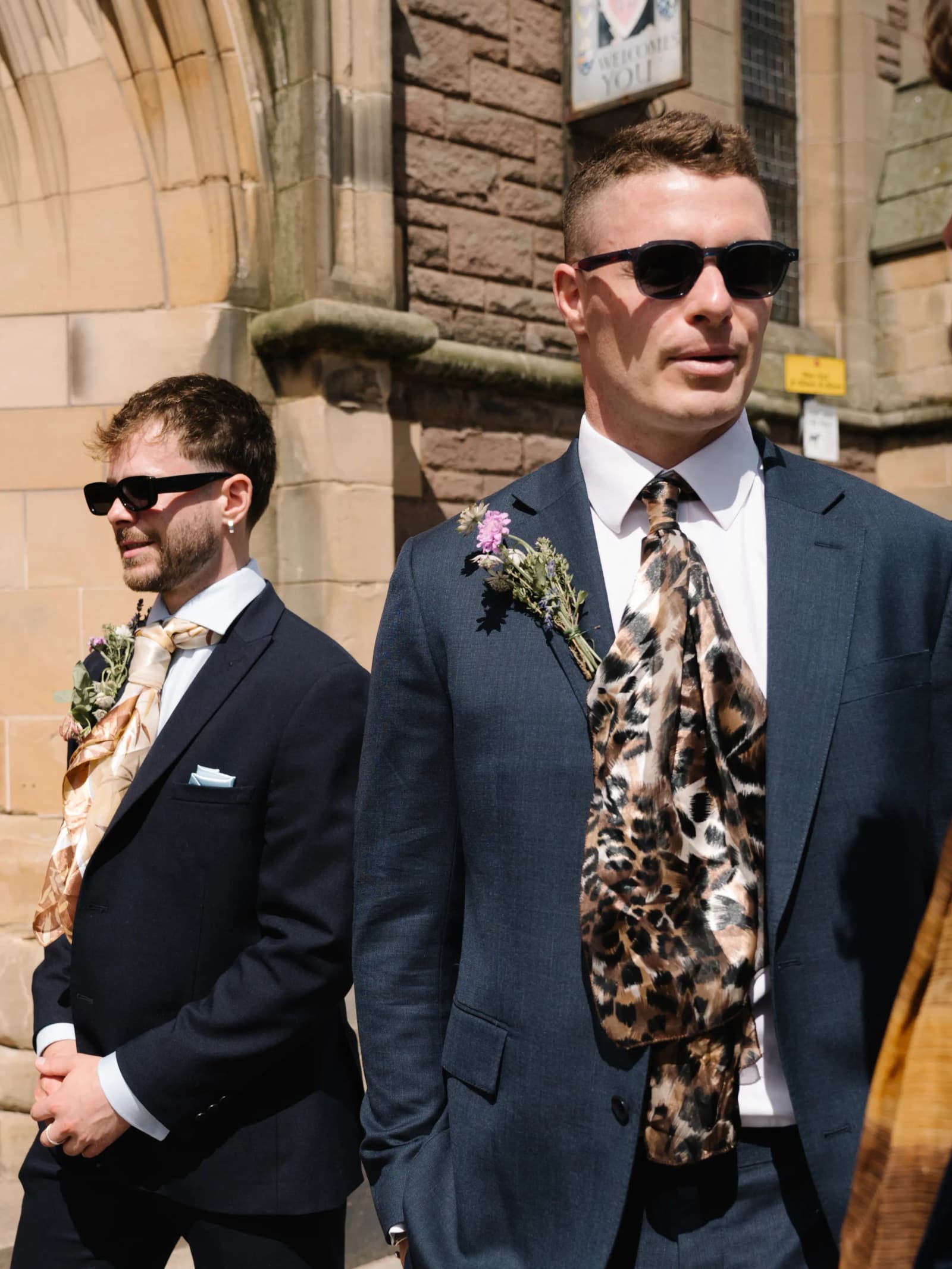 Groomsmen in navy suits and sunglasses wearing gold and brown vintage silk scarves as ties outside a church in Forfar