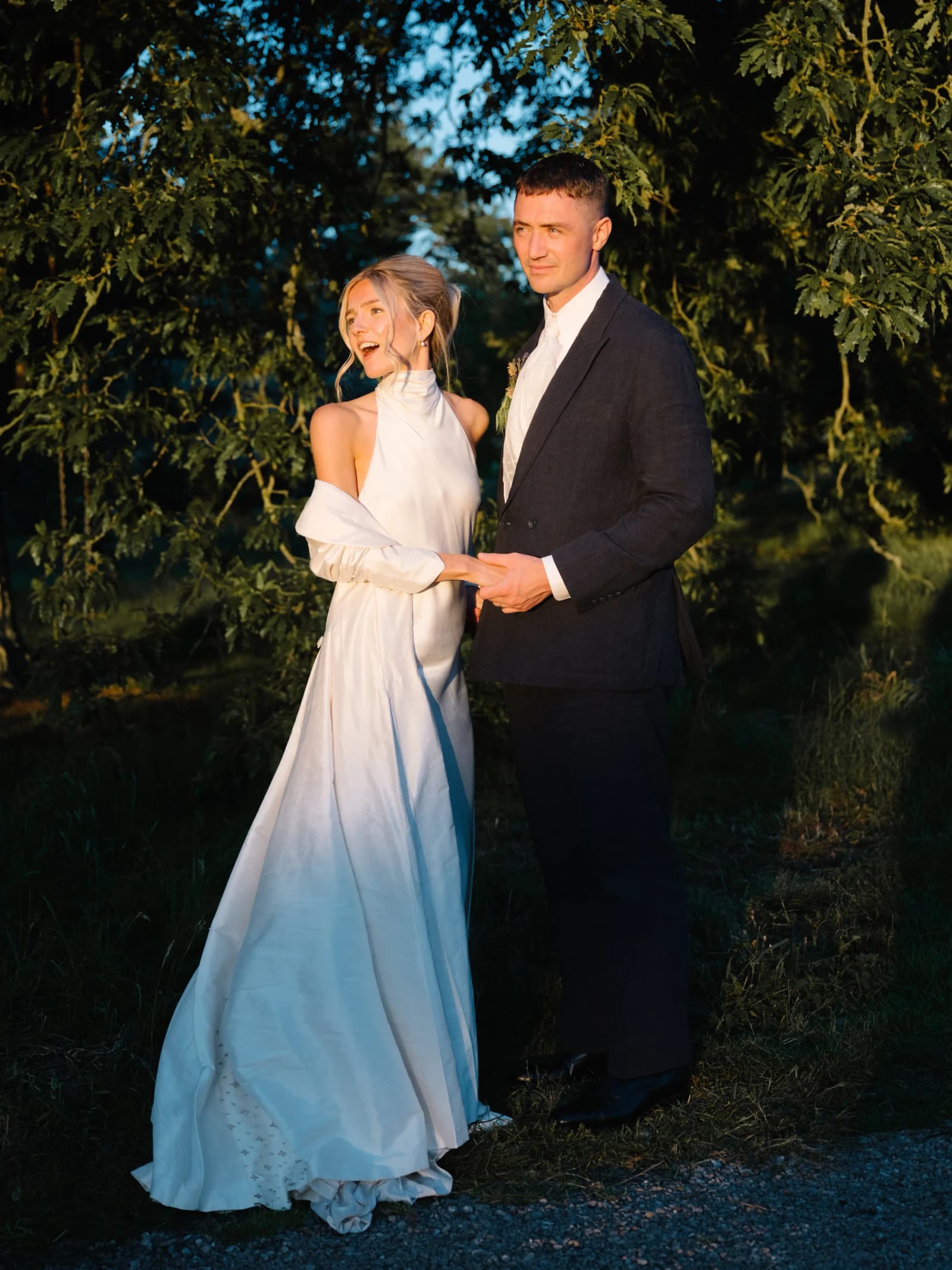 Bride in a satin halterneck gown and groom holding hands at golden hour in the grounds of Middleton House, Scotland