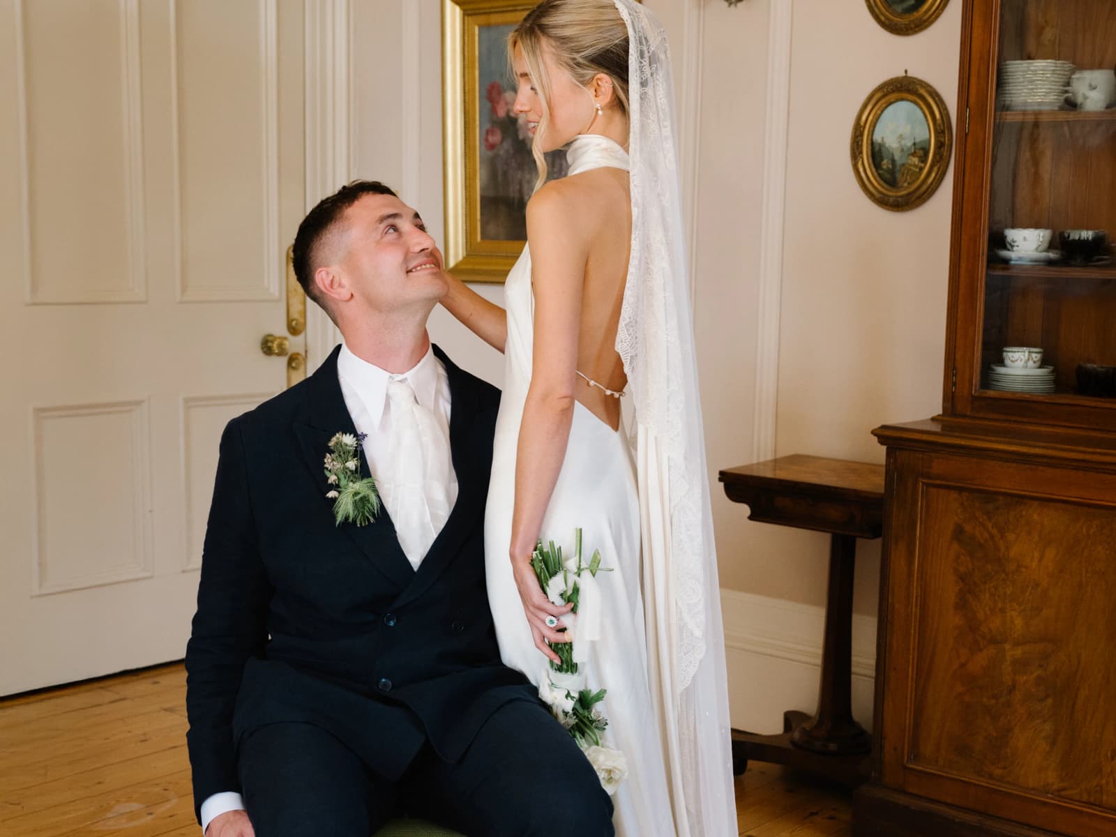Groom smiling up at his bride in her backless gown and lace-edged veil in the drawing room at Middleton House, Scotland